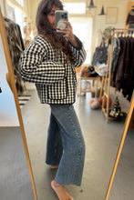 Load image into Gallery viewer, Person taking a mirror selfie wearing a black and white checkered jacket and blue jeans in a clothing store.