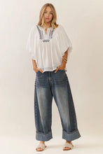 Load image into Gallery viewer, Woman wearing a white embroidered top and blue jeans on a plain background