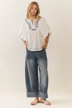 Load image into Gallery viewer, Woman wearing a white embroidered top and blue jeans on a plain background