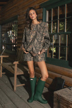 Load image into Gallery viewer, Woman in camouflage outfit with green boots standing on a wooden porch.