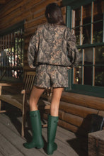 Load image into Gallery viewer, Person wearing a camouflage outfit with green boots on a wooden porch.