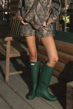 Load image into Gallery viewer, Person wearing camouflage outfit with green rain boots on a wooden porch.