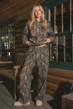 Load image into Gallery viewer, Woman wearing a camouflage outfit standing in front of a wooden cabin.