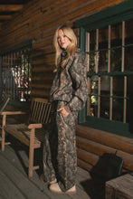 Load image into Gallery viewer, Woman in camouflage outfit standing on a wooden porch.