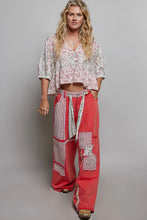 Load image into Gallery viewer, Woman wearing a floral top and red patchwork pants on a gray background