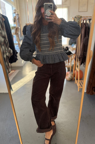 Person taking a mirror selfie wearing a textured sweater and brown pants in a clothing store.