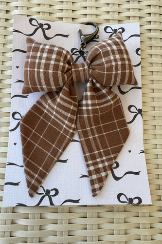 Brown plaid hair bow on a white card with black designs, placed on a woven surface.