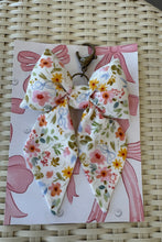 Load image into Gallery viewer, Floral-patterned keychain on a matching card with pink ribbons on a woven surface