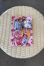 Load image into Gallery viewer, Decorative bow on a pink card with floral patterns, placed on a woven surface.