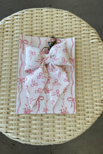 Load image into Gallery viewer, Woven basket with a white fabric with red patterns and a hair tie on a gray surface