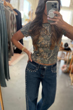 Load image into Gallery viewer, Person taking a mirror selfie wearing a camouflage top and blue jeans in a store.