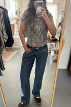 Load image into Gallery viewer, Person wearing a patterned top and blue jeans in front of a mirror.