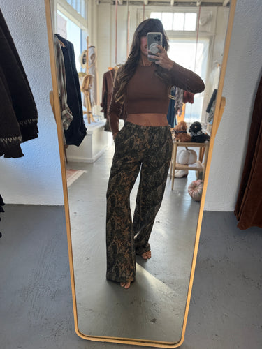Person taking a mirror selfie wearing a brown top and camouflage pants in a room with a large mirror.