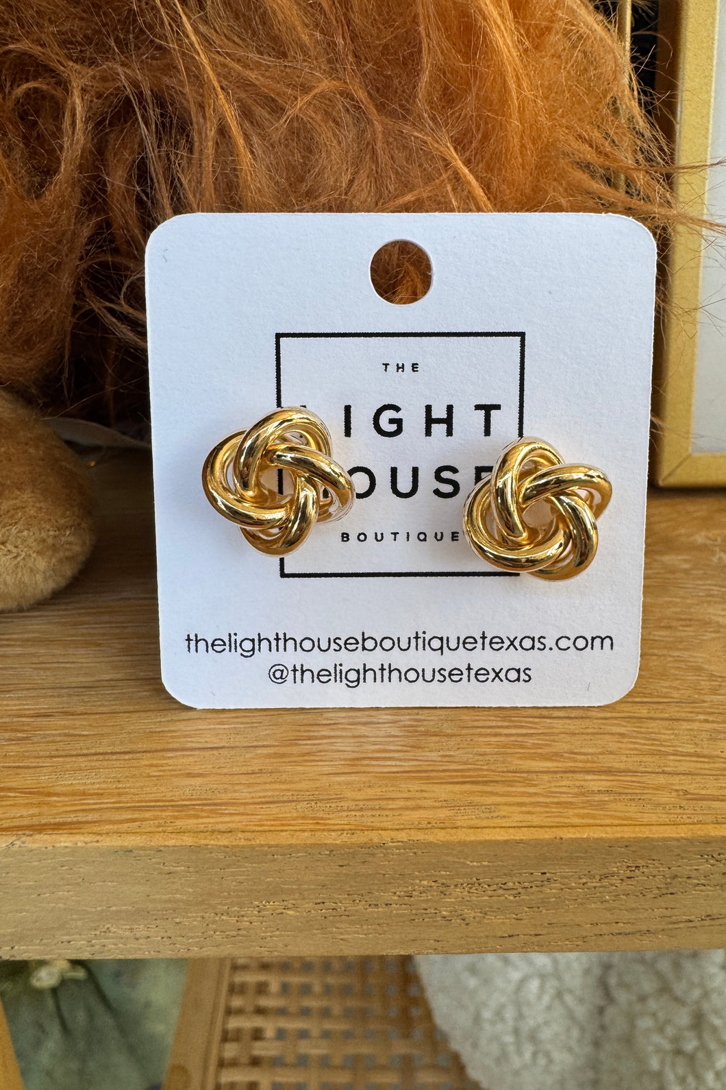 Gold knot earrings on a branded card with a wooden background