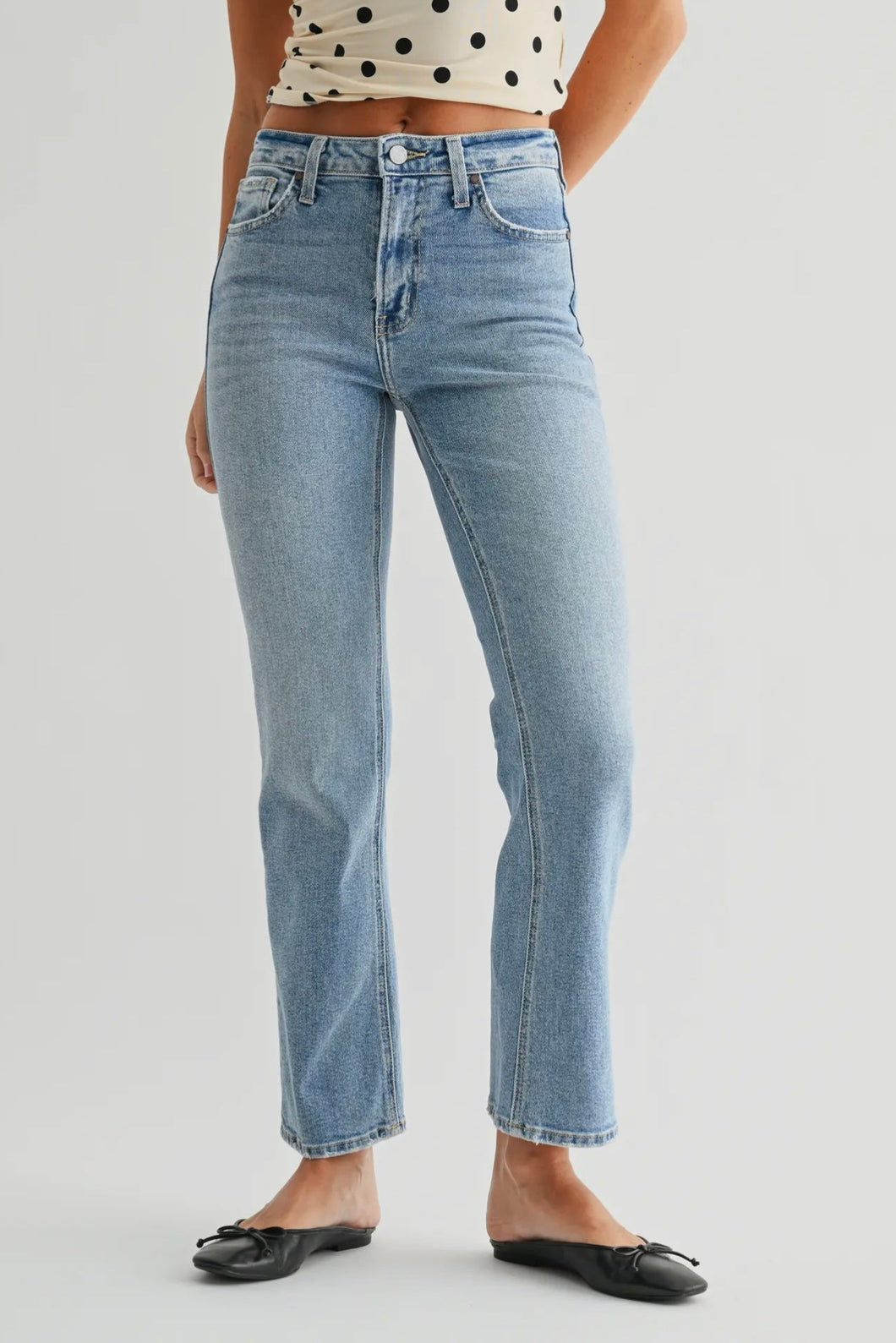 Person wearing light blue jeans and a polka dot top on a plain background