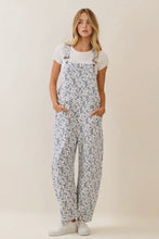Load image into Gallery viewer, Woman wearing floral overalls and a white t-shirt on a beige background
