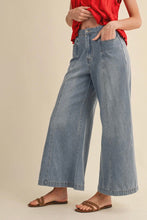 Load image into Gallery viewer, Person wearing blue wide-leg jeans and a red top on a beige background