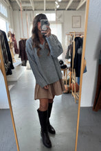 Load image into Gallery viewer, Person taking a mirror selfie wearing a gray sweater, beige pleated skirt, and black knee-high boots in a clothing store.