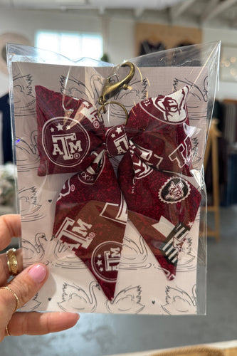 Packaged hair bow with visible branding held by a hand in an indoor setting.