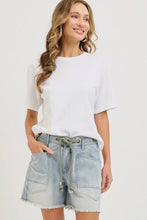 Load image into Gallery viewer, Woman wearing a white t-shirt and denim shorts on a plain background