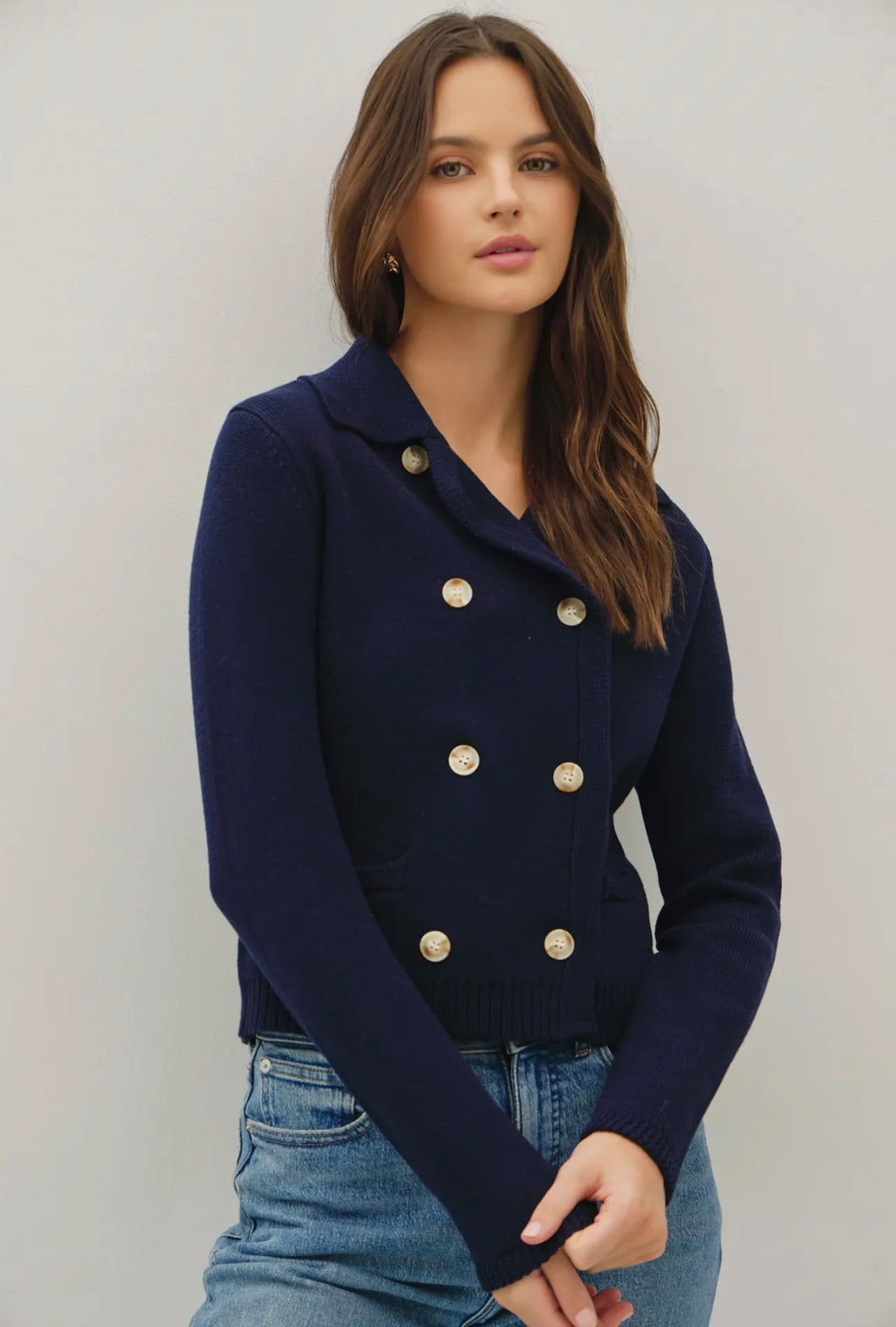 Woman wearing a navy blue cardigan with gold buttons against a plain background