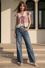 Load image into Gallery viewer, Woman wearing a polka dot top and blue jeans standing on steps outside a building.