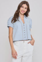 Load image into Gallery viewer, Woman wearing a light blue denim shirt with white pants on a plain background