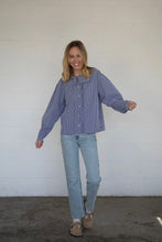 Load image into Gallery viewer, Woman wearing a blue checkered shirt and light blue jeans against a white wall.