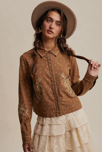 Woman wearing a brown embroidered blouse and beige hat against a neutral background