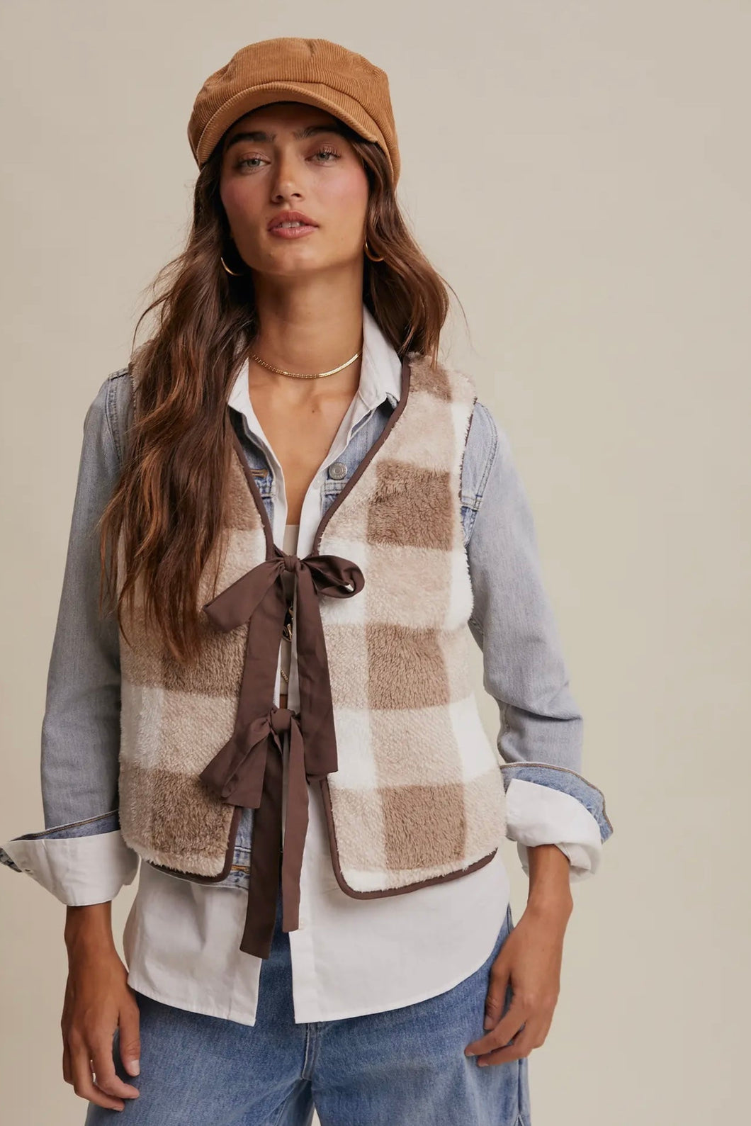 Woman wearing a plaid vest, shirt, jeans, and cap on a beige background