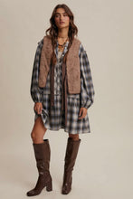Load image into Gallery viewer, Woman wearing a plaid dress with a brown vest and knee-high boots on a beige background