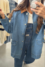 Load image into Gallery viewer, Person wearing a denim jacket and overalls taking a mirror selfie in a clothing store.