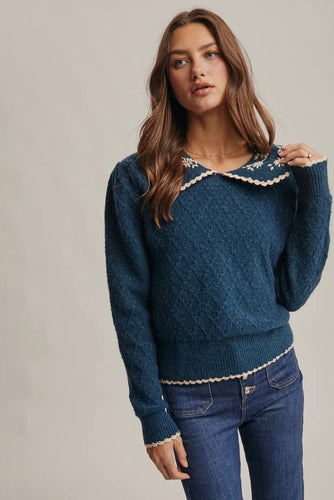 Woman wearing a blue sweater with lace details on a plain background
