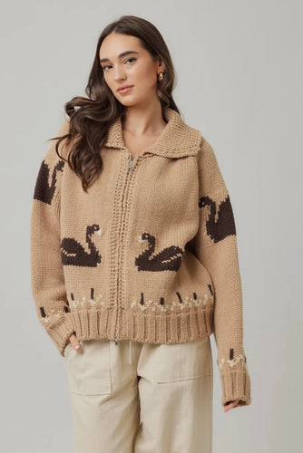 Woman wearing a beige knit cardigan with black swan designs on a plain background