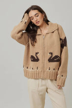 Load image into Gallery viewer, Woman wearing a beige knitted cardigan with black swan designs on a plain background