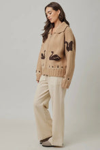 Load image into Gallery viewer, Woman wearing a beige knitted cardigan with black Swan designs on a plain background