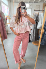 Load image into Gallery viewer, Woman taking a mirror selfie wearing a floral top and pink pants in a clothing store.