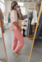 Load image into Gallery viewer, Person taking a mirror selfie wearing a floral top and pink pants in a clothing store.