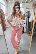 Load image into Gallery viewer, Woman taking a mirror selfie wearing a floral top and pink pants in a clothing store.