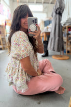 Load image into Gallery viewer, Woman taking a mirror selfie in a floral top and pink pants in a store.