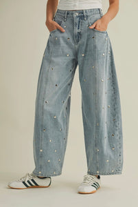 Person wearing light blue denim jeans with decorative studs on a neutral background
