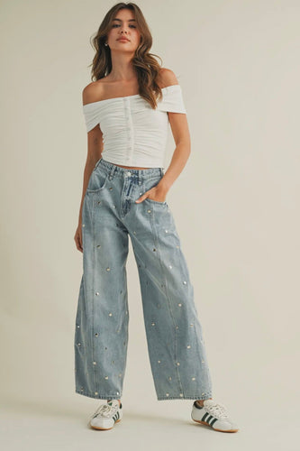 Woman wearing a white off-shoulder top and light blue jeans with decorative elements on a beige background