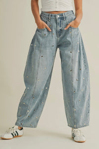 Light blue denim pants with decorative studs worn by a person on a beige background