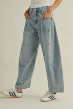 Load image into Gallery viewer, Person wearing light blue jeans with decorative studs and white sneakers on a beige background