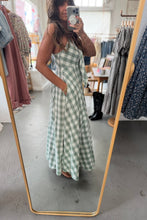 Load image into Gallery viewer, Woman in a green checkered dress standing in front of a mirror in a clothing store.