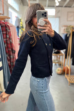 Load image into Gallery viewer, Person wearing a navy jacket and light blue jeans taking a mirror selfie in a clothing store.
