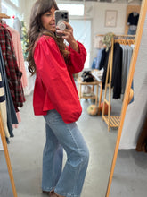 Load image into Gallery viewer, Woman taking a mirror selfie wearing a red top and blue jeans in a clothing store.