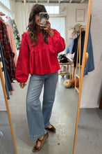 Load image into Gallery viewer, Person taking a mirror selfie wearing a red blouse and blue jeans in a clothing store.