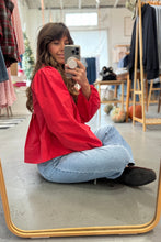 Load image into Gallery viewer, Person taking a mirror selfie wearing a red shirt and blue jeans in a clothing store.