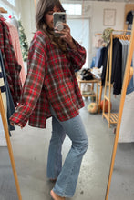 Load image into Gallery viewer, Person wearing a red plaid shirt and blue jeans taking a mirror selfie in a clothing store.
